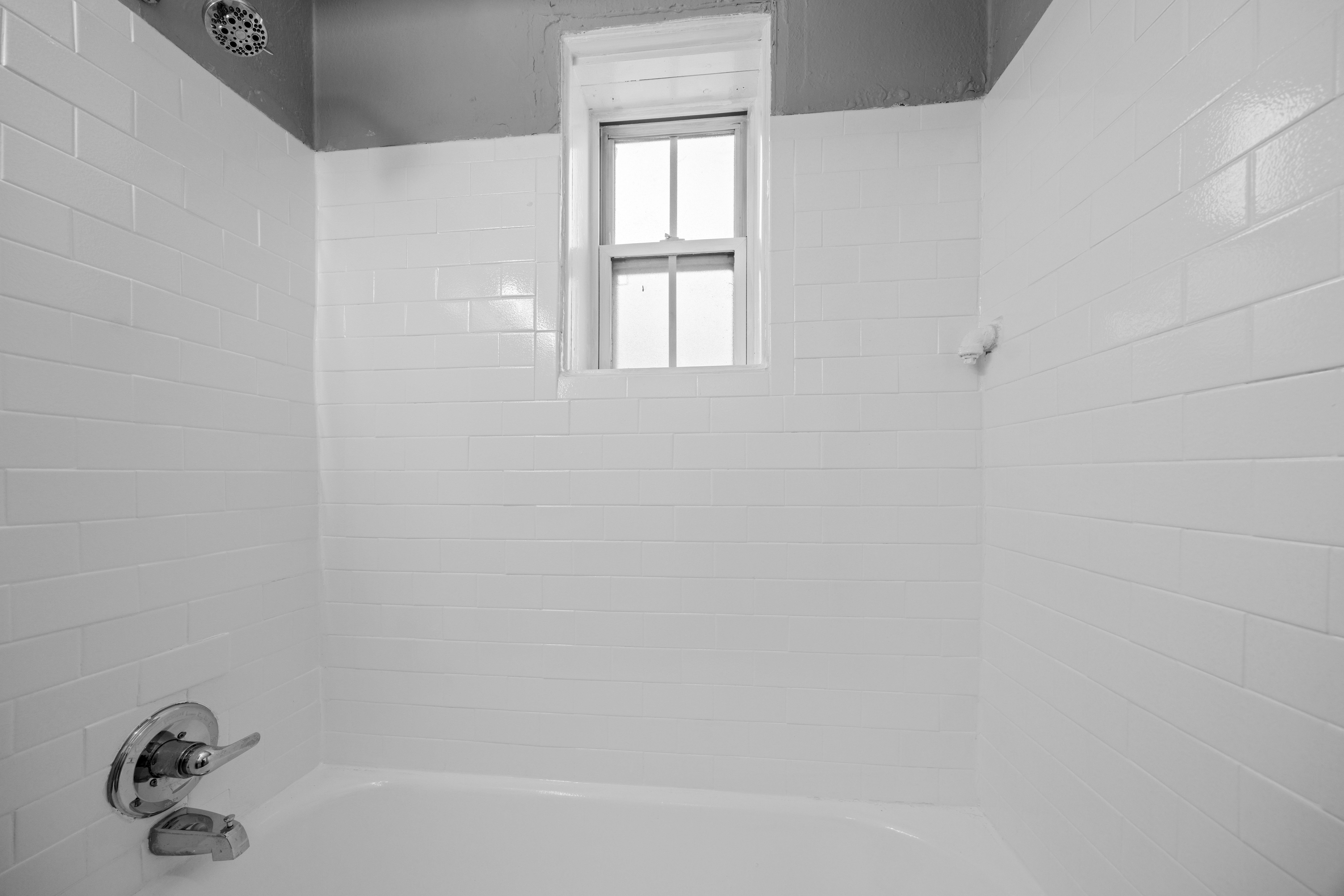 A white tiled bathroom with a window.
